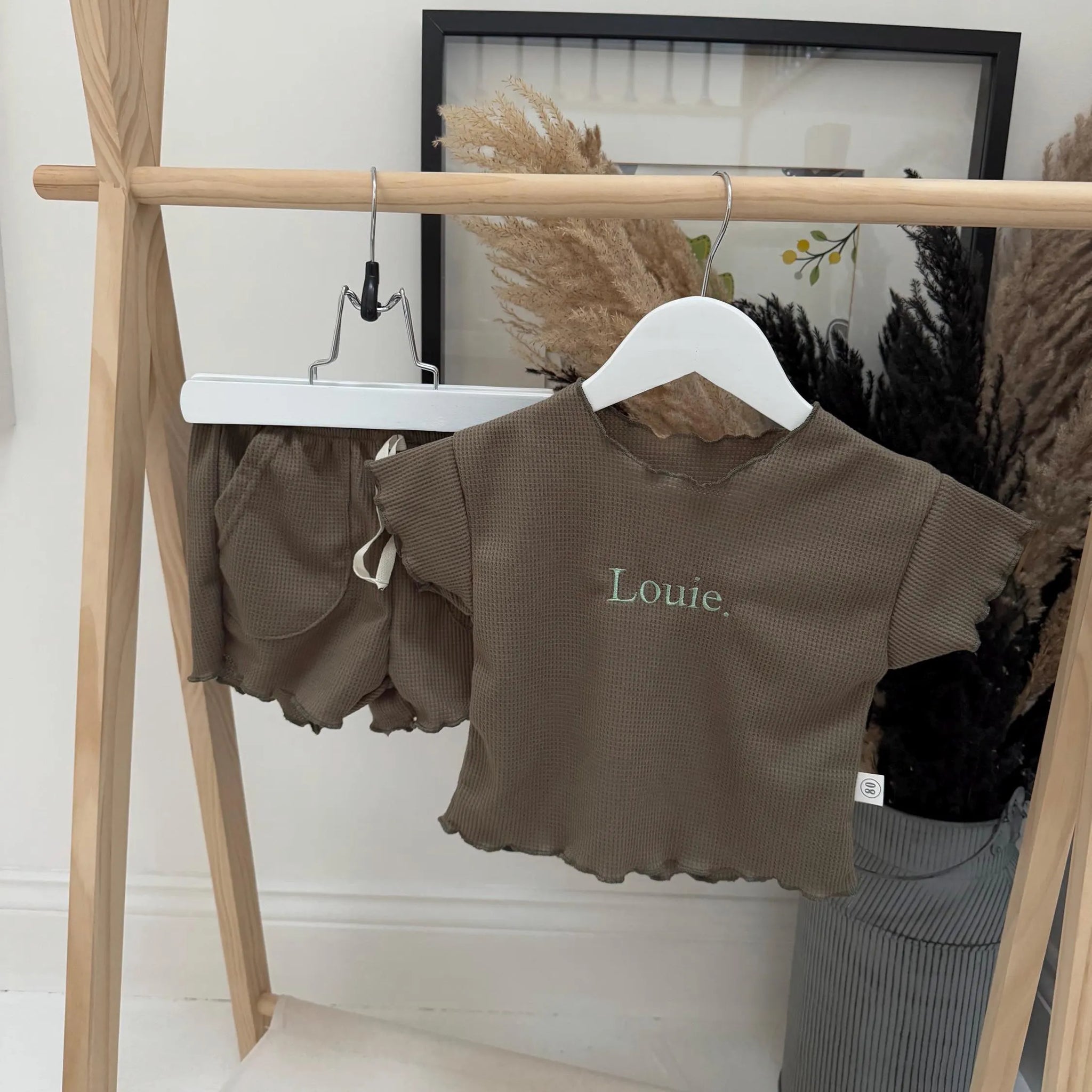 Children's brown outfit with 'Louie' on a hanger against a white wall.