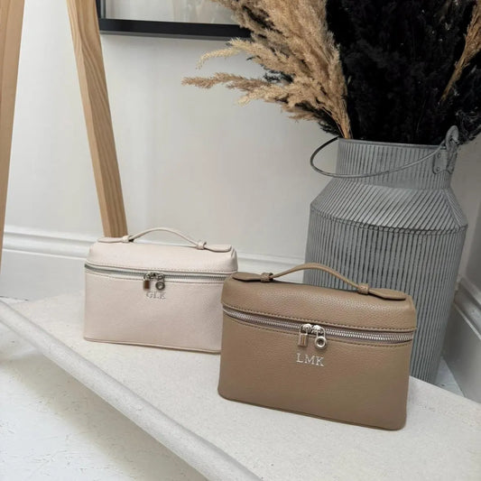 Two mini hand bags on a white surface with a vase of dried plants in the background. Personalised
