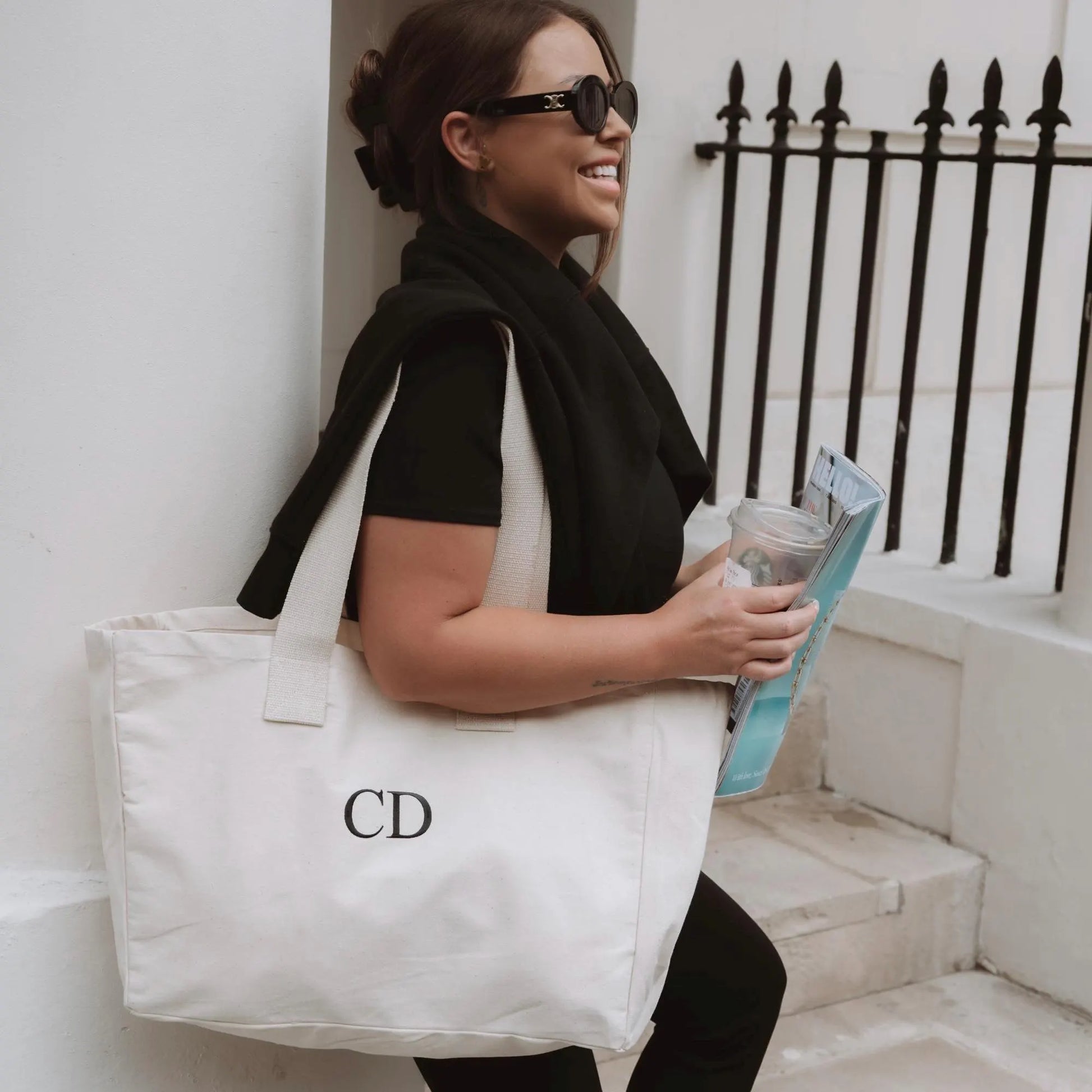 Woman holding a white tote bag with 'CD' initials, standing outdoors.