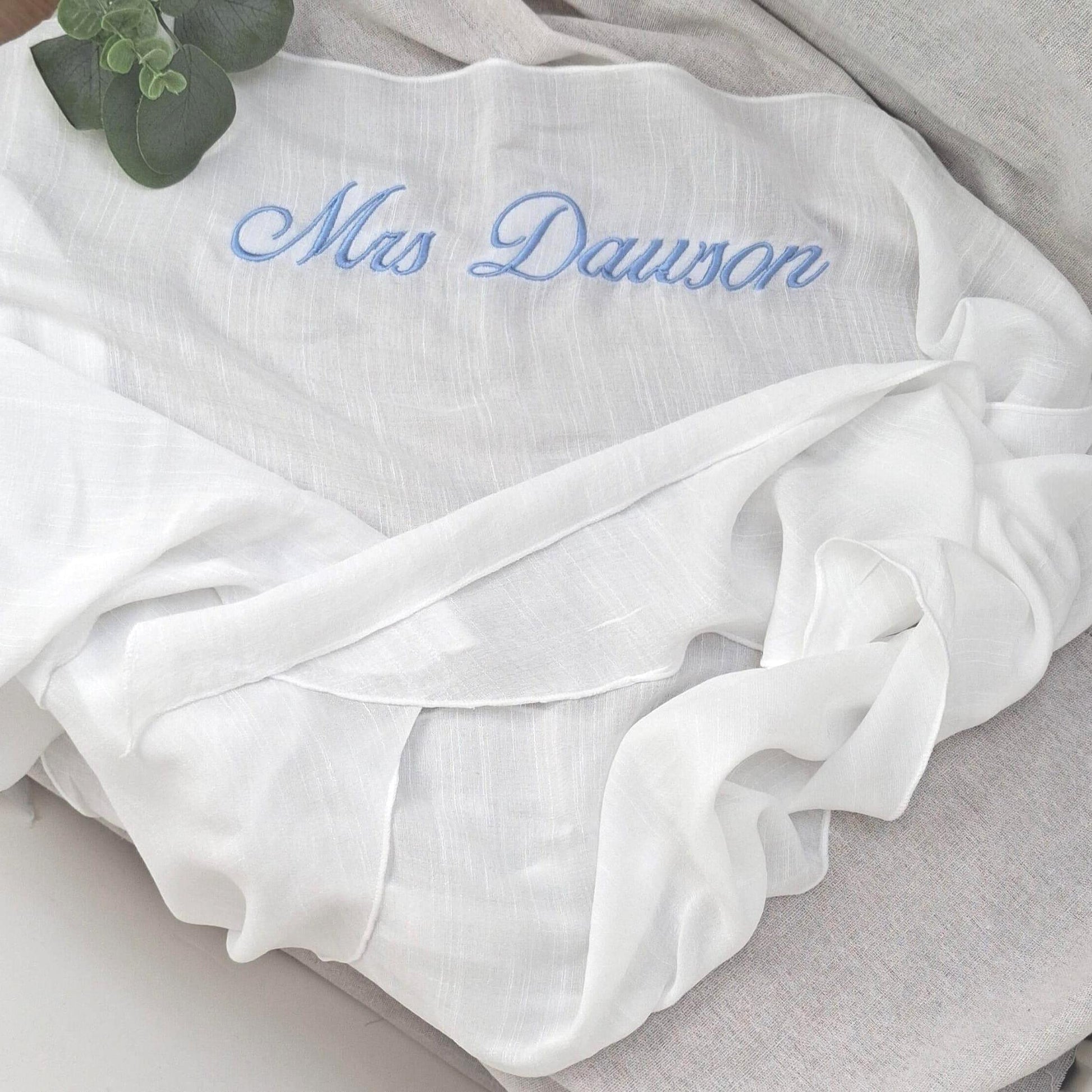 White sarong  with 'Mrs Dawson' embroidered in blue on a light gray surface.