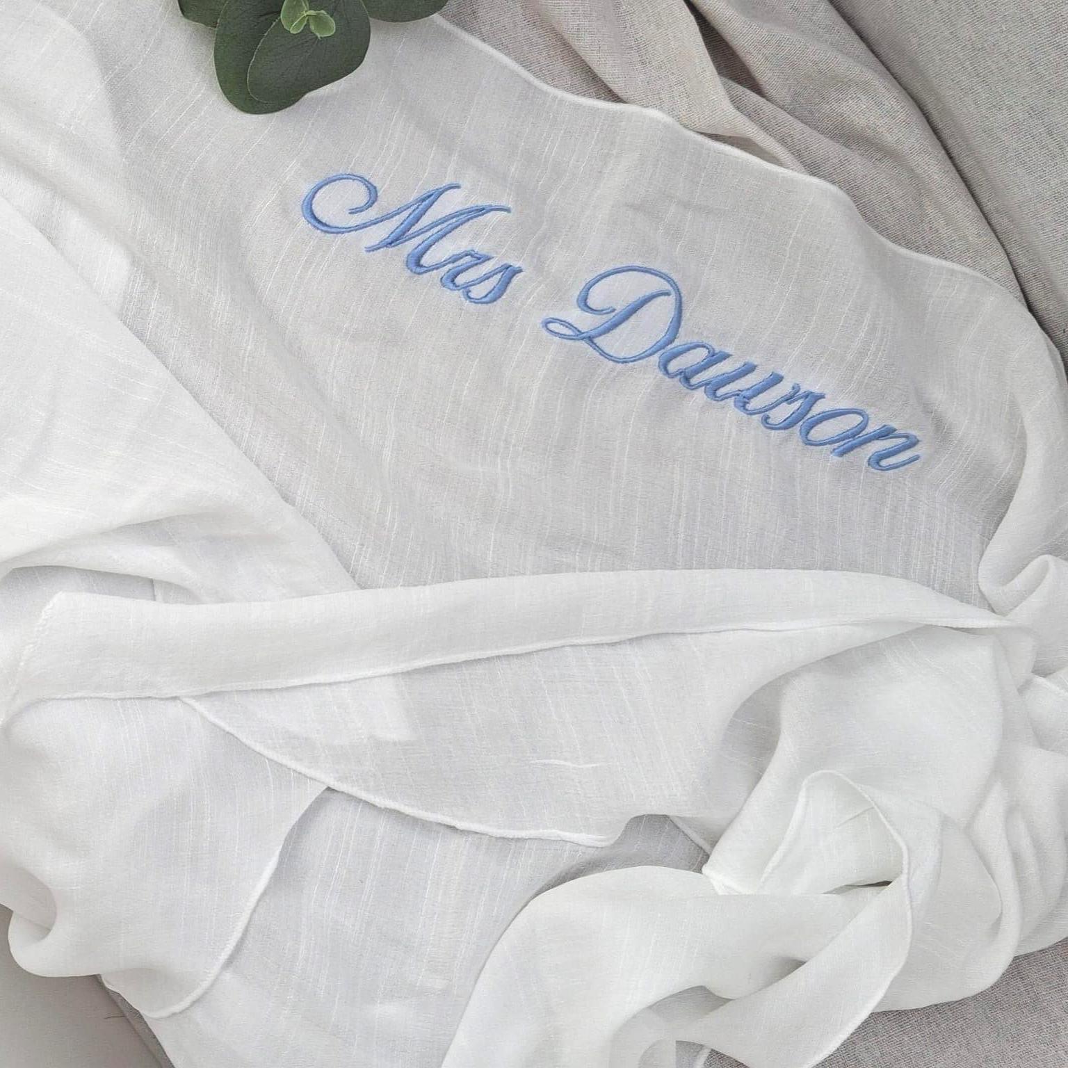 White sarong with blue embroidered text 'Mrs. Dawson' on a neutral background