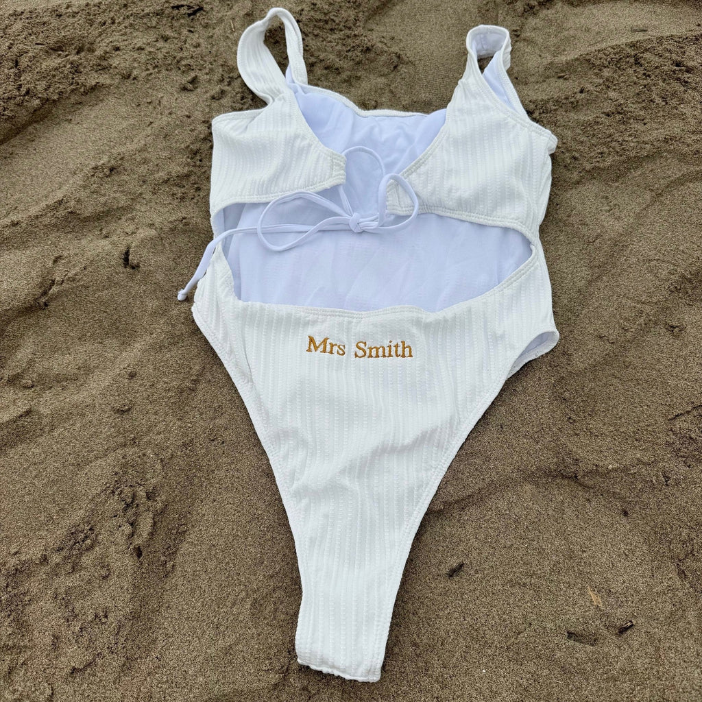 White swimsuit with 'Mrs Smith' embroidery on sand 