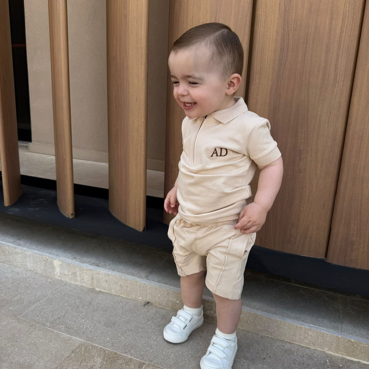 Child in a beige outfit with 'AD' on a wooden background