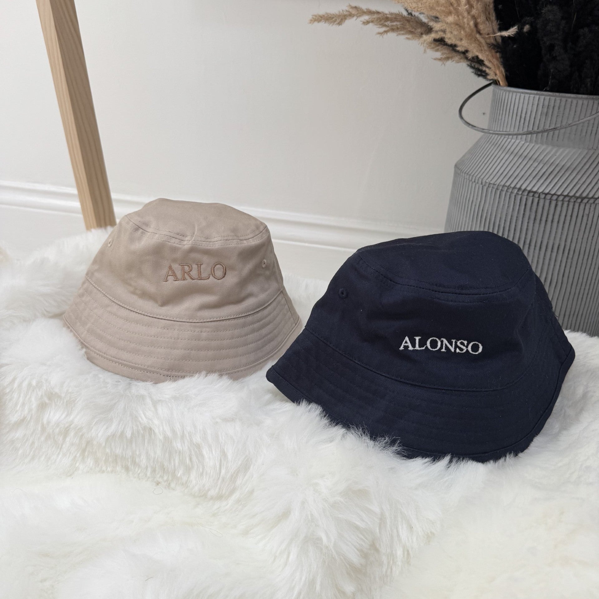 Two kids bucket hats, one beige and one navy, with 'ALONSO' and "ARLO" personalisation on a white surface.
