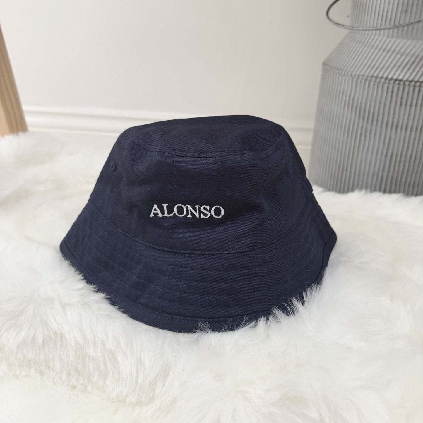 Navy bucket hat with 'ALONSO' branding on a white fluffy surface.
