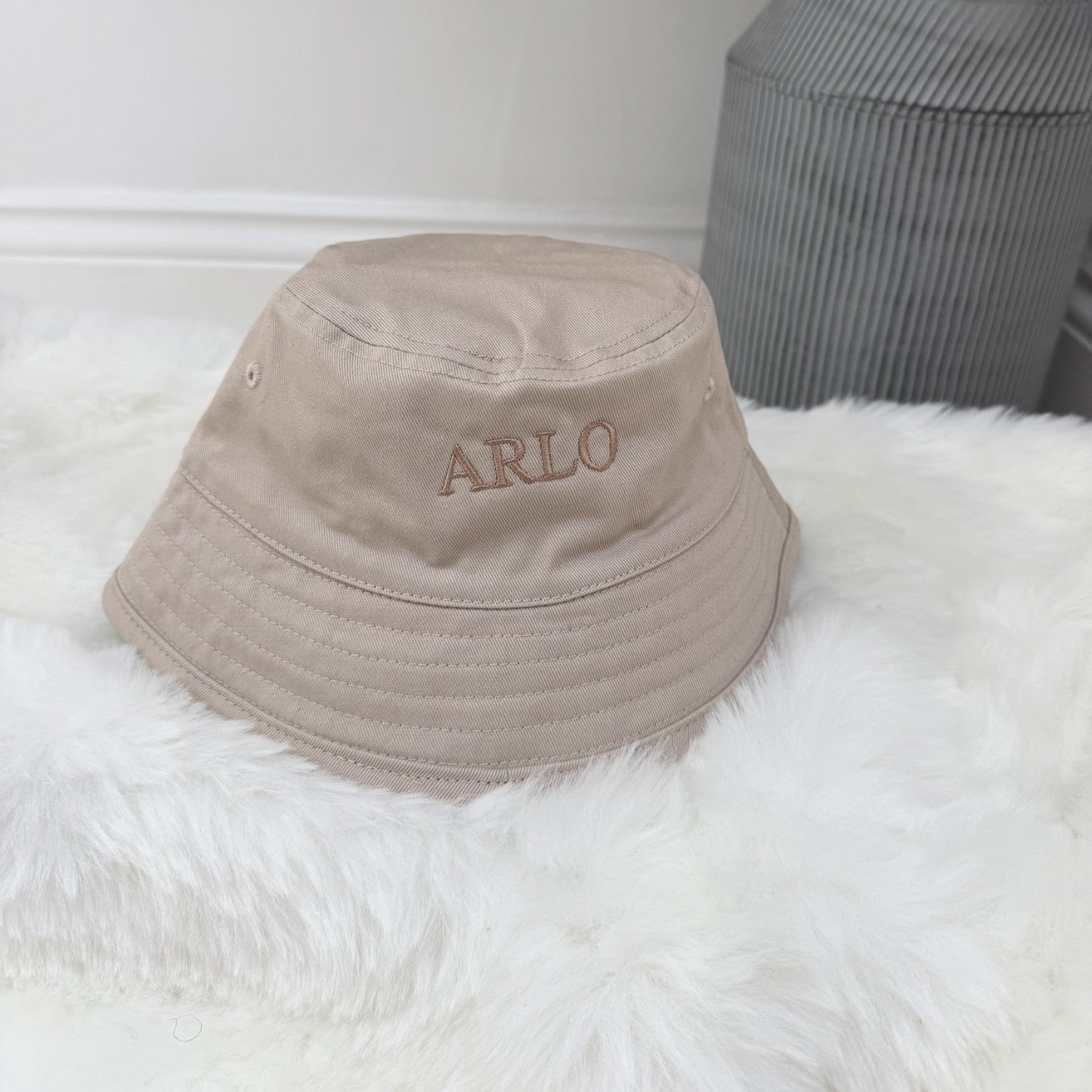 Beige bucket hat with 'ARLO' embroidery on a white surface.