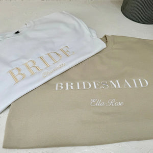 Two sweatshirts, one white with 'BRIDE' and another beige with 'Bridesmaid', on a light surface.