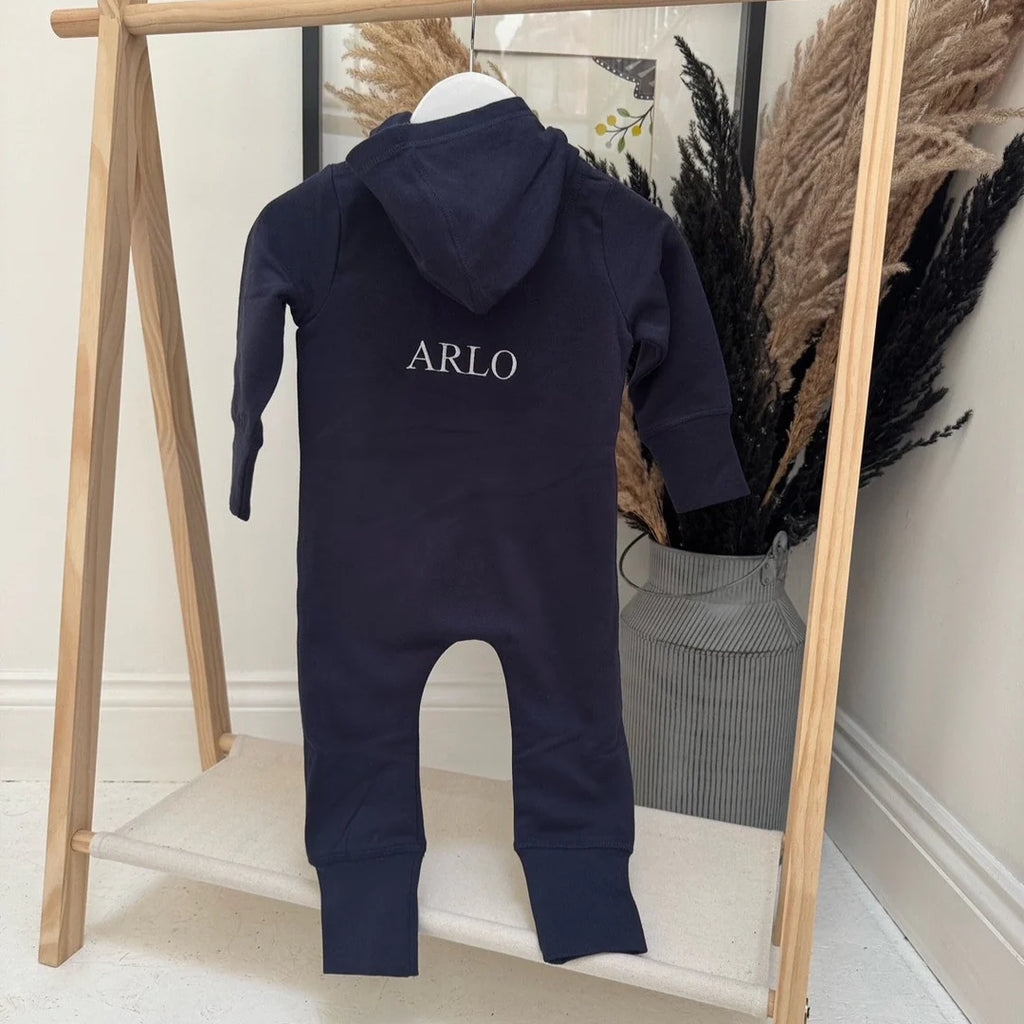 Navy blue baby onesie with 'ARLO' branding on a wooden rack.