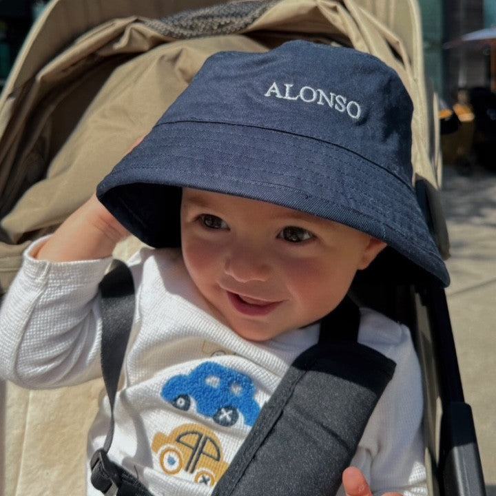 Baby wearing a blue hat with 'ALONSO' embroidered on it, sitting in a stroller.