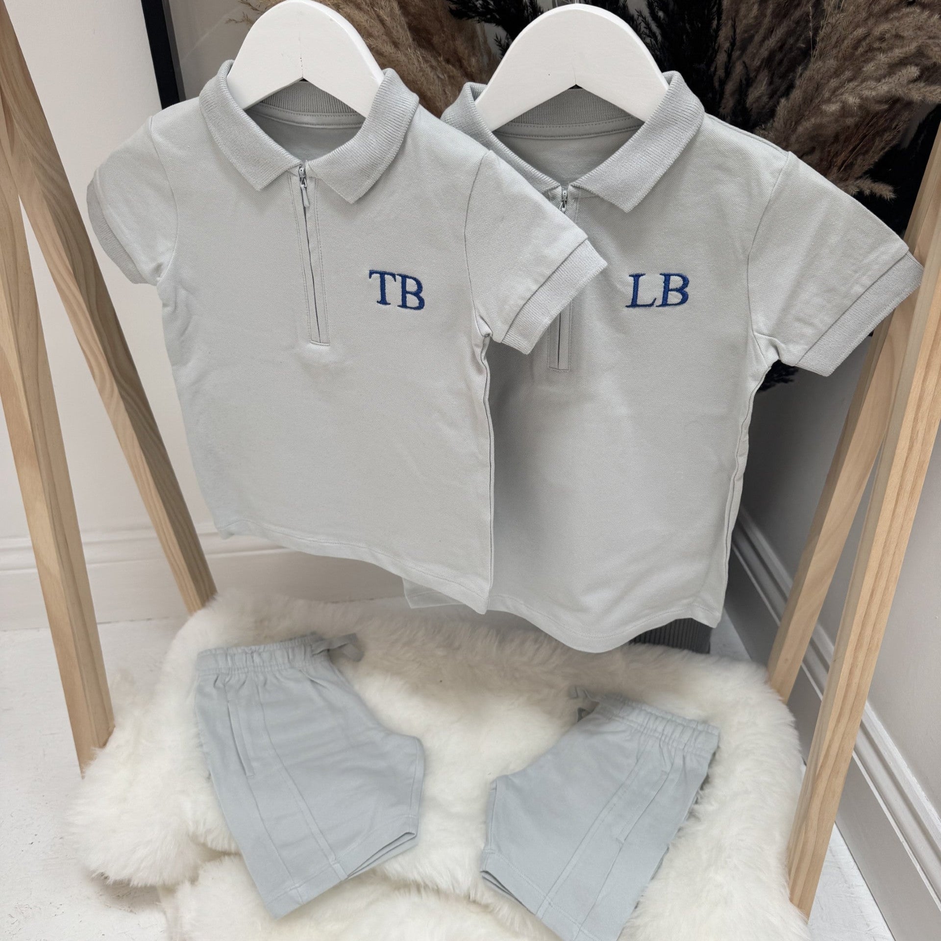 Two grey polo shirts with embroidered initials on hangers on a wooden rack.
