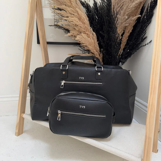 Black duffel bag with 'TVS' branding on a wooden stand against a neutral wall.