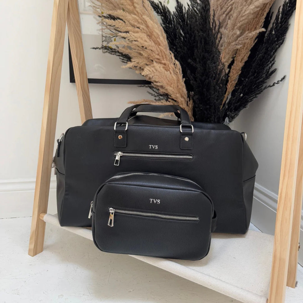 Black duffel bag with 'TVS' branding on a wooden stand against a neutral wall.