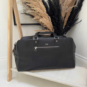 Black duffel bag with 'TVS' branding on a wooden shelf.