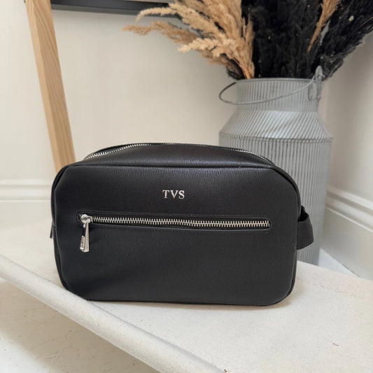 Black bag with 'TVS' monogram on a white surface with decorative elements.