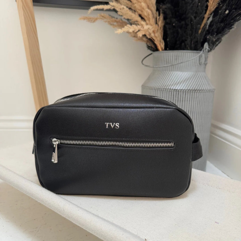 Black bag with 'TVS' monogram on a white surface with decorative elements.