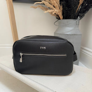 Black bag with 'TVS' monogram on a white surface with decorative elements.