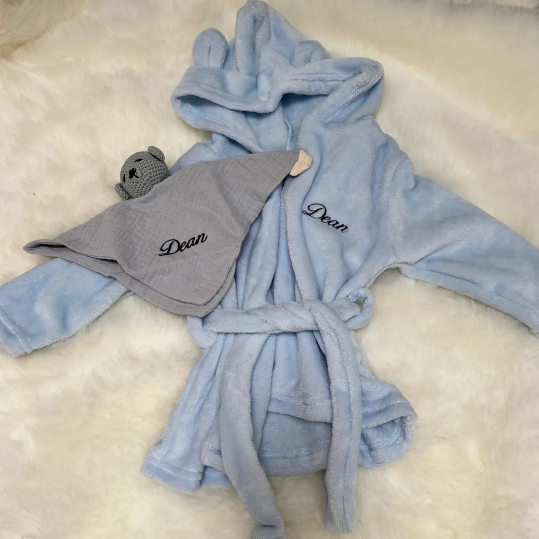 Blue robe with hood and blue soothing towel with ´Dean' on a beige surface