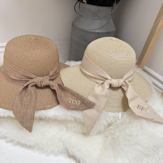 Two straw hats with ribbons on a white surface, with decorative elements in the background. Both personalised