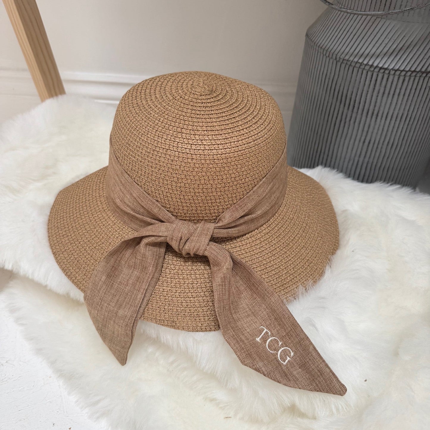 Brown straw hat with a bow on a white surface with initials TCG