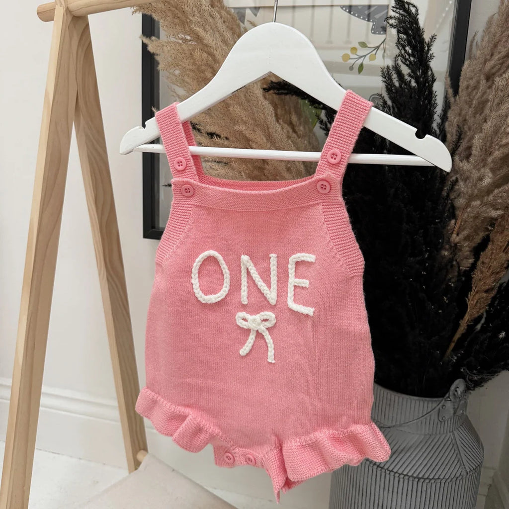 Pink baby romper with 'ONE' and bow design on a hanger.