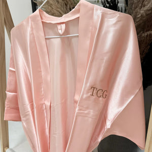 Pink satin robe with 'TCG' embroidery on a hanger.