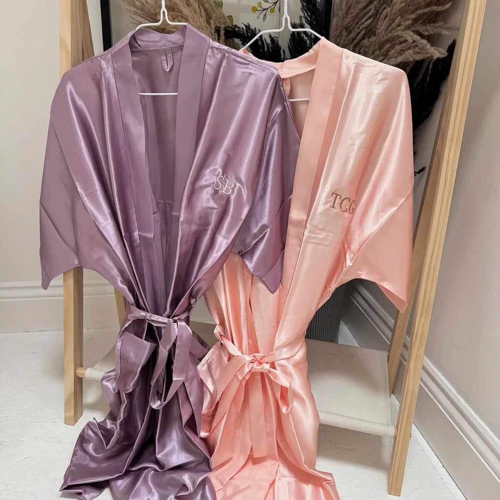 Two satin robes, one purple and one pink, hanging on a wooden rack.