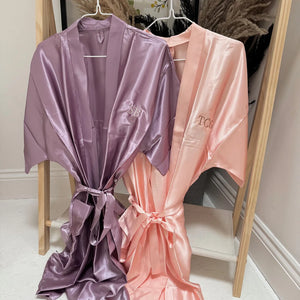 Two satin robes, one purple and one pink, hanging on a wooden rack.