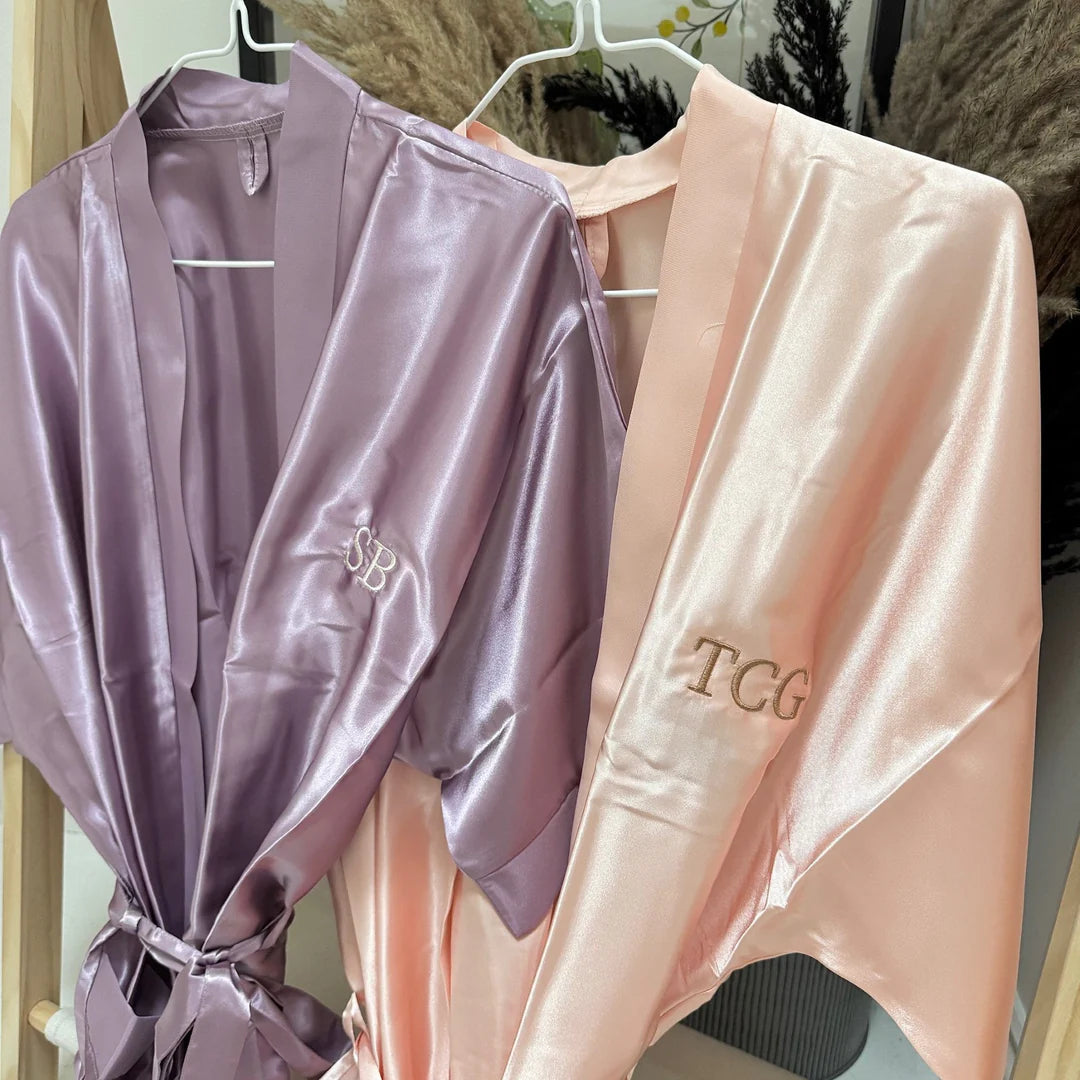 Two satin robes, one purple and one pink, with visible branding on a hanger.