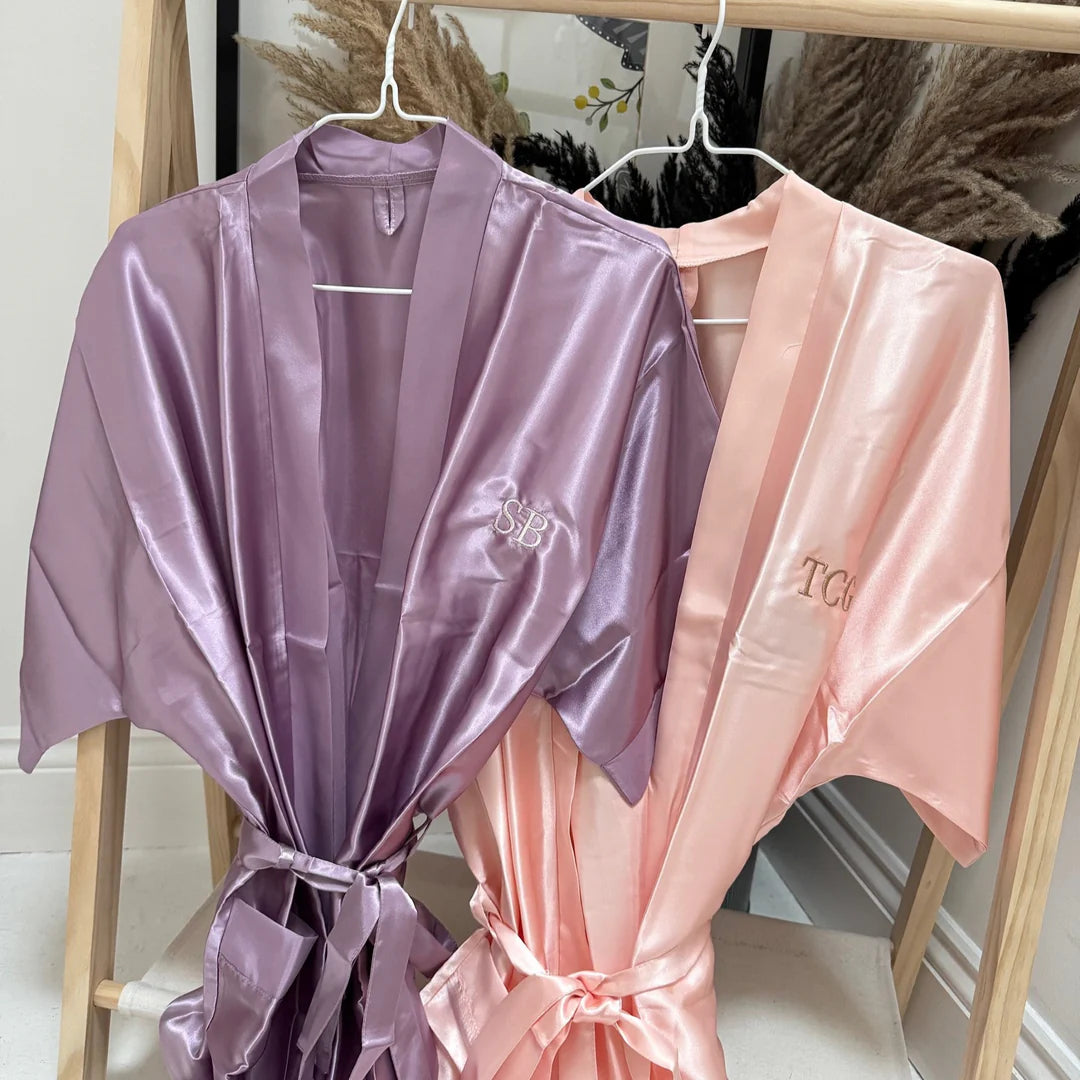 Two satin robes, one purple and one pink, hanging on a rack.