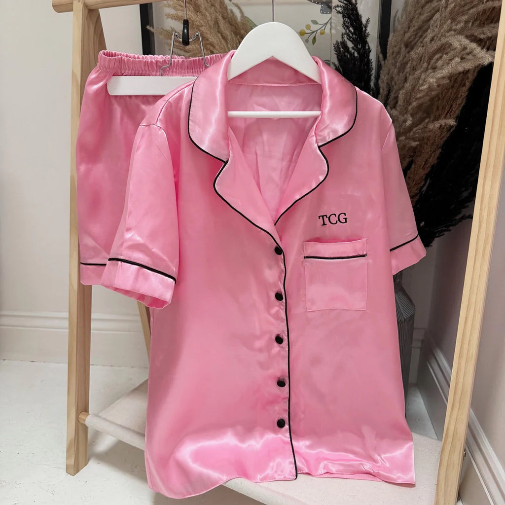 Pink satin pajama set with black piping on a wooden rack.