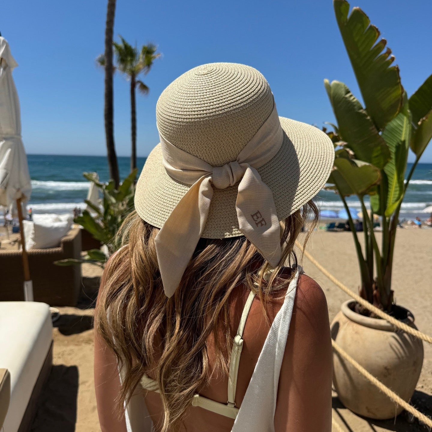 Woman wearing a large sun hat on a beach with palm trees and ocean in the background