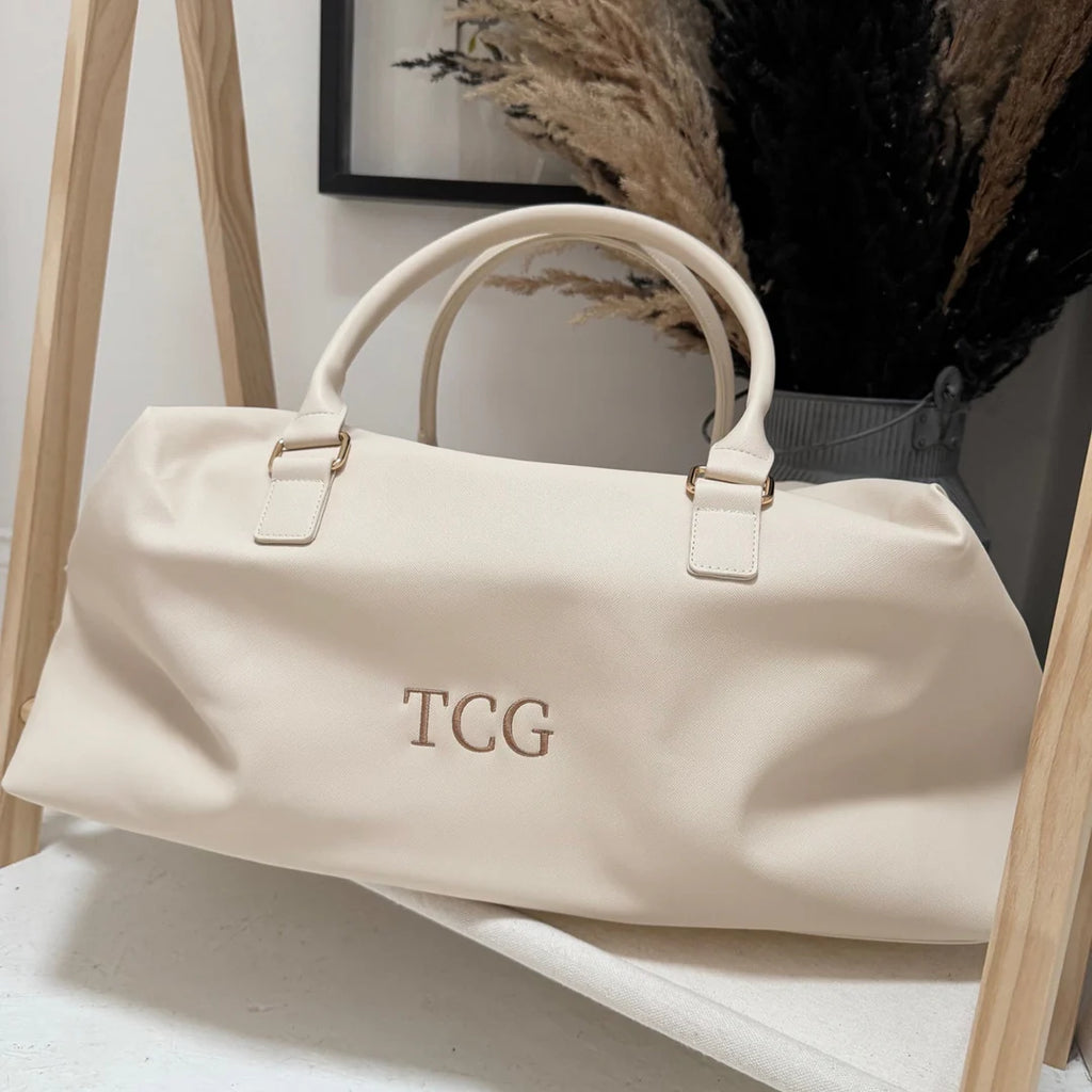 Beige handbag with 'TCG' monogram on a light surface with a blurred background