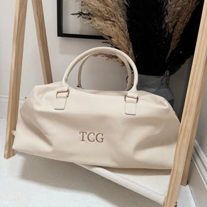 beige weekend bag with the initials TCG on it