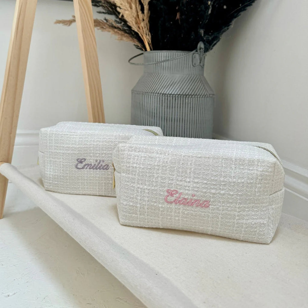 Two textured pouches with embroidered names on a white surface.