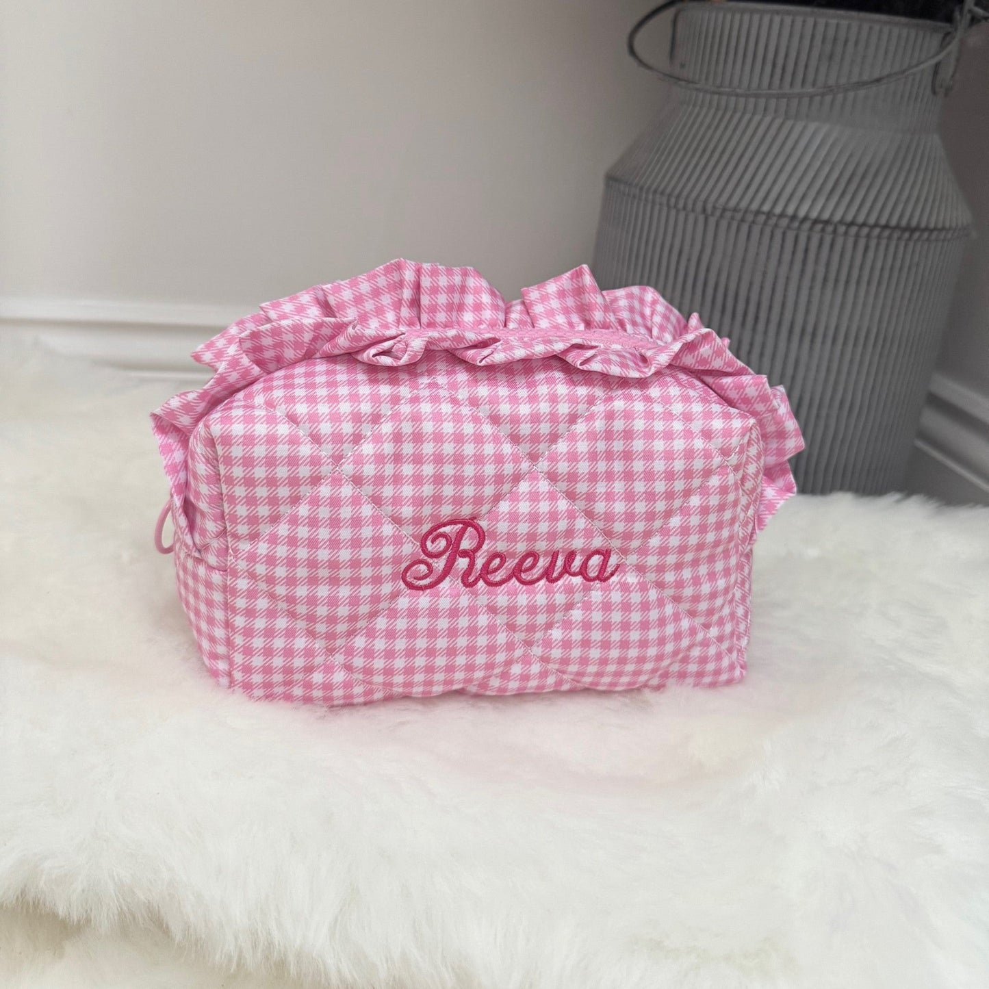 Pink gingham bag with 'Reeva' embroidery on a white surface with decorative elements.