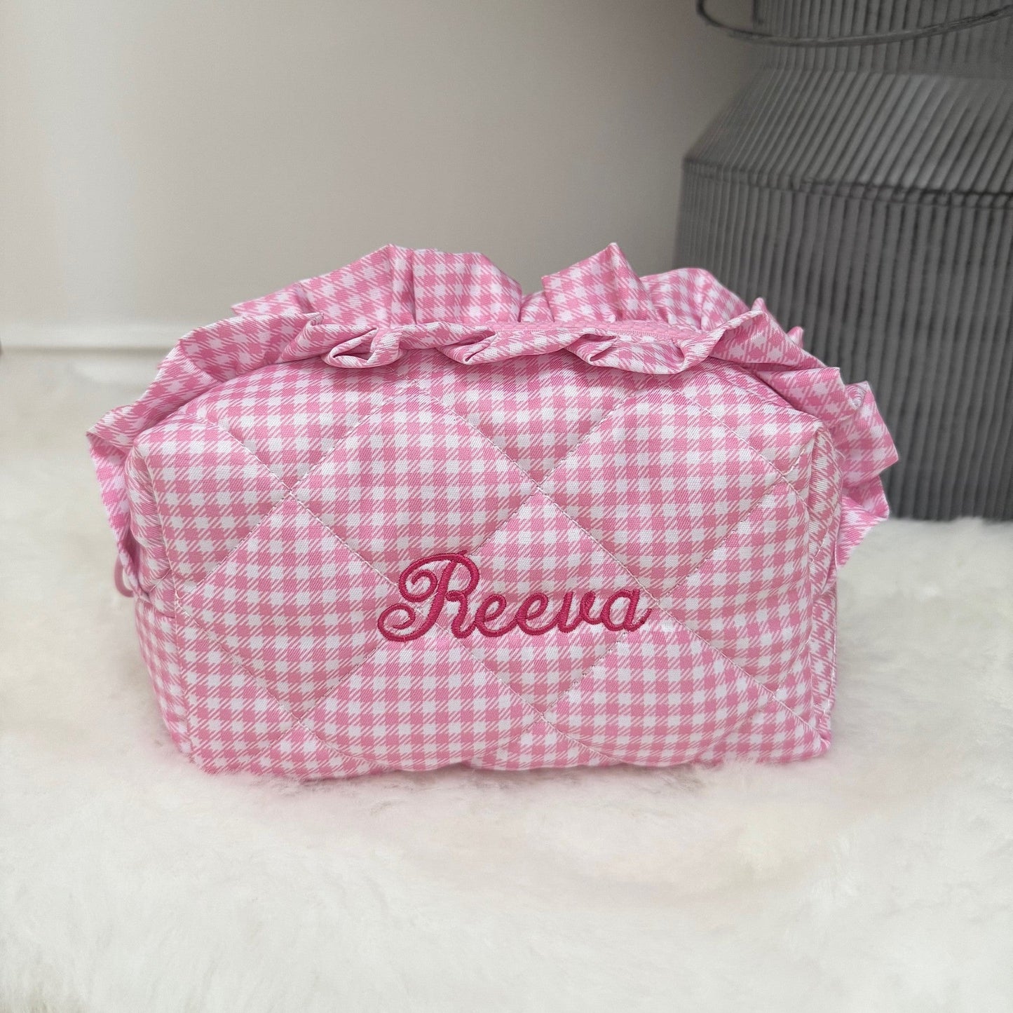 Pink gingham make up bag with 'Reeva' embroidery on a white surface.