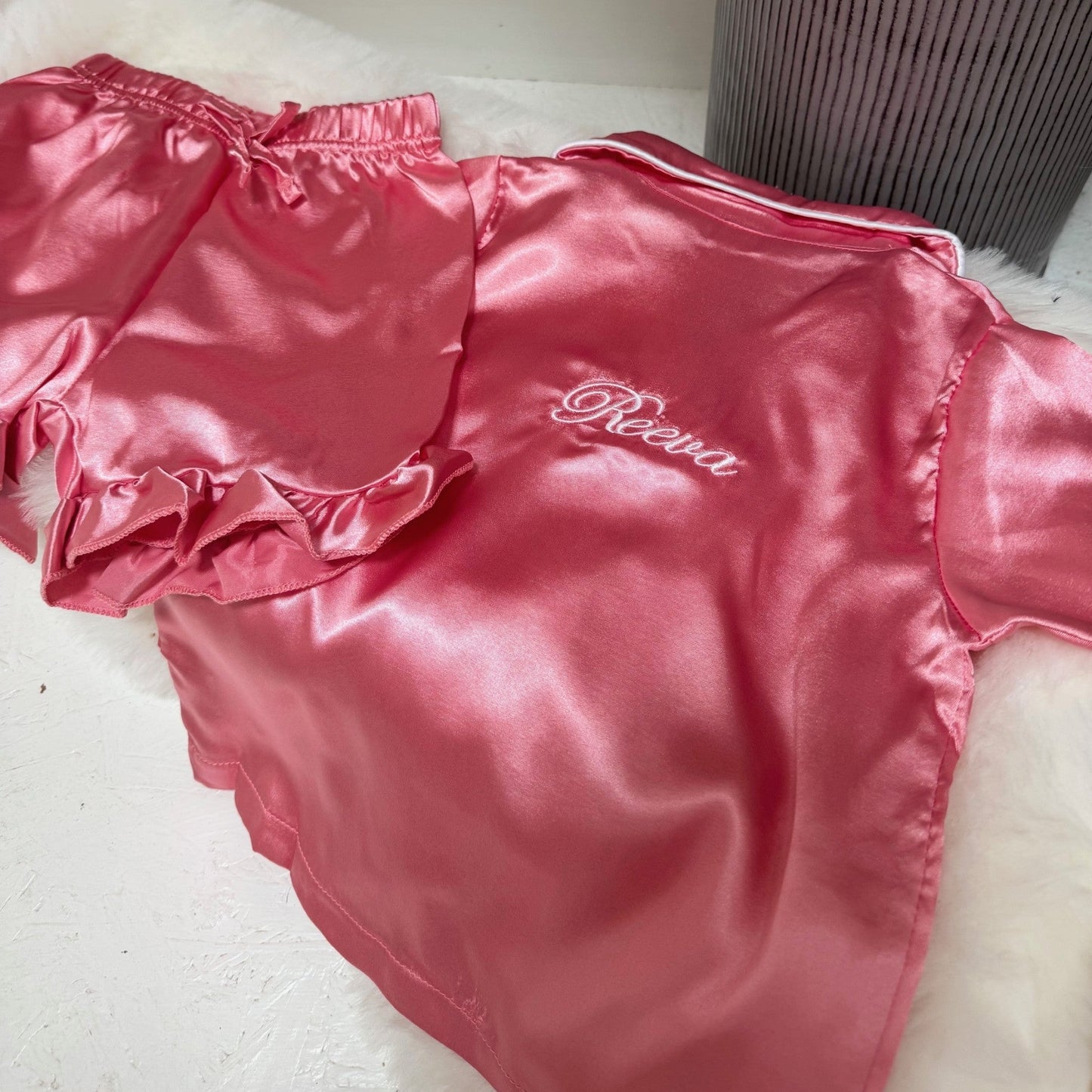 Pink satinpjs with 'Reeva'personalisation on a white surface.
