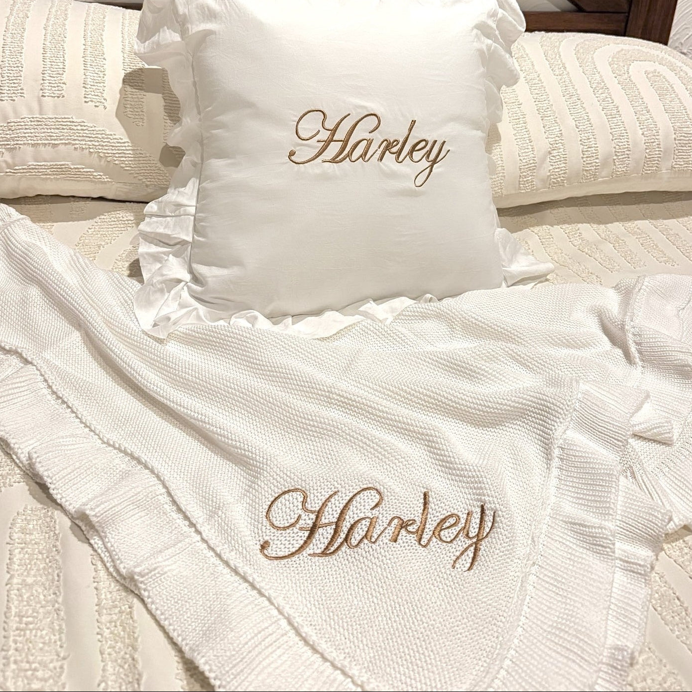 White pillow and blanket with 'Harley' embroidery on a bed with wooden headboard.