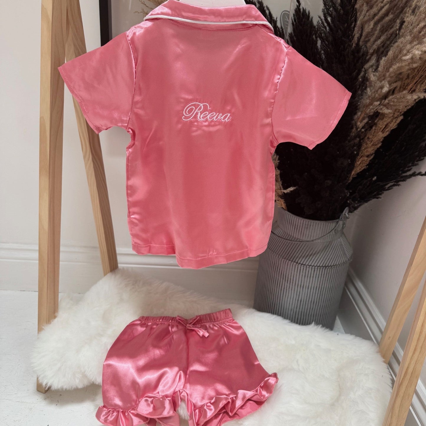 Pink satin pjs with 'Reeva' branding on a wooden rack.