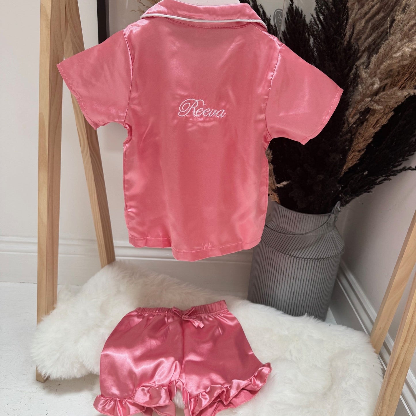Pink satin pjs with 'Reeva' branding on a wooden rack.