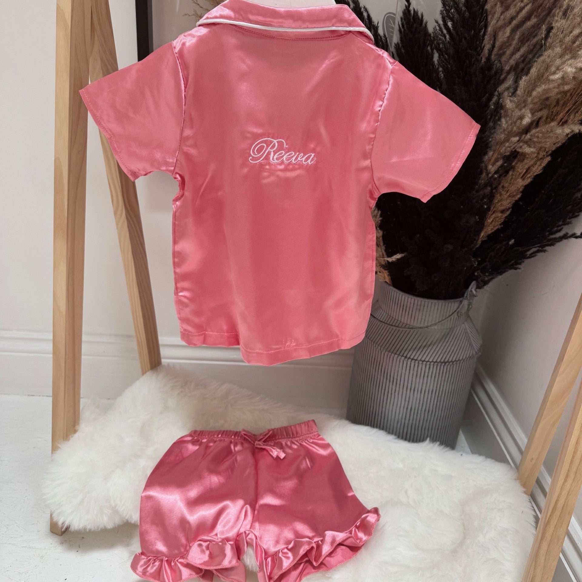 Pink satin pjs with 'Reeva' branding on a wooden rack.