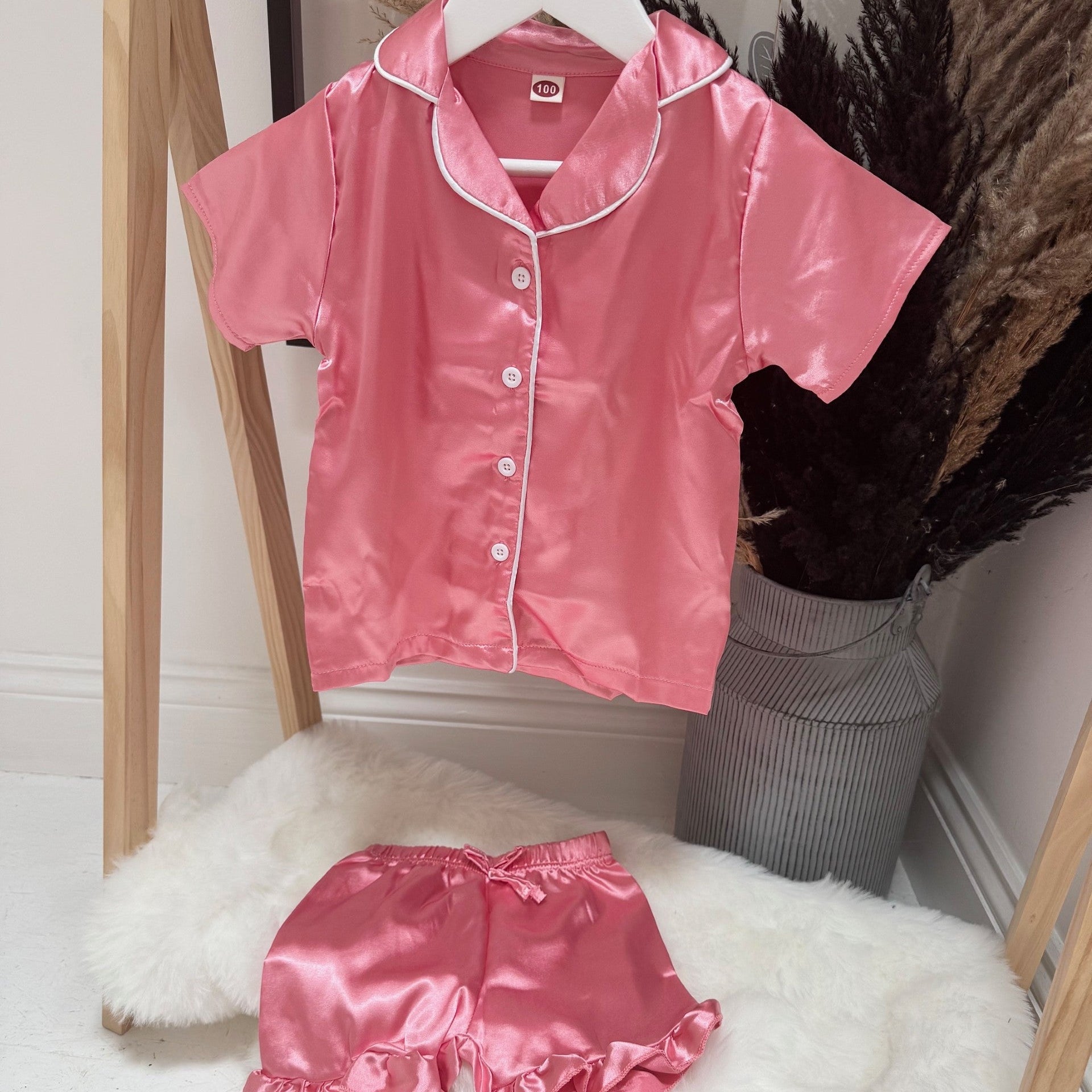 Pink satin pajama set on a hanger against a neutral background