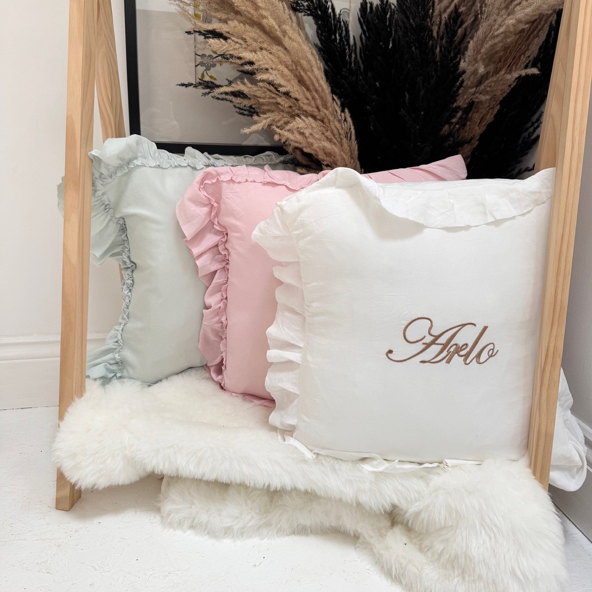 Decorative custom pillows on a fur surface with a wooden frame and pampas grass in the background.