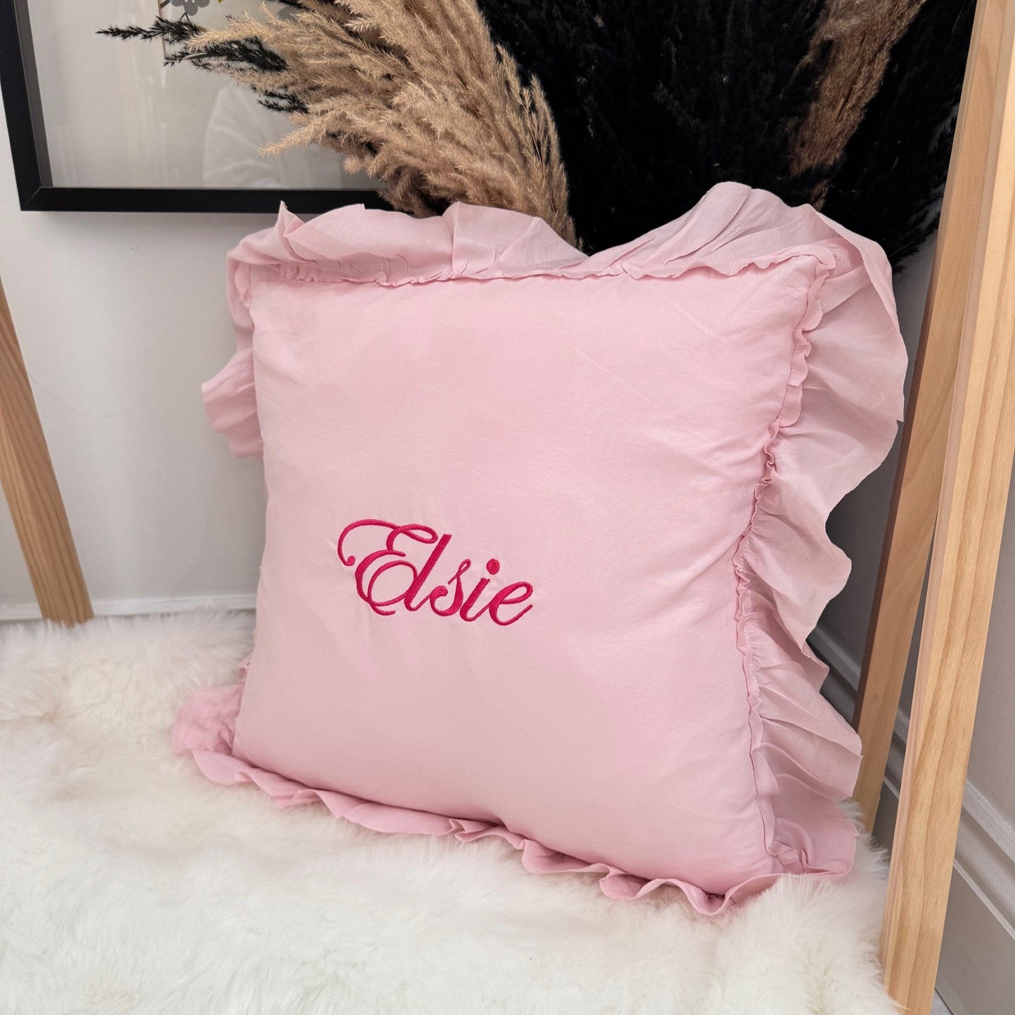 Pink pillow with 'Elsie' embroidery on a white surface with decorative elements.
