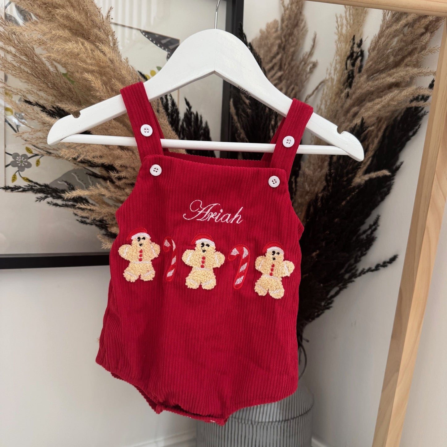 Red baby romper with gingerbread design on a hanger against a decorative background