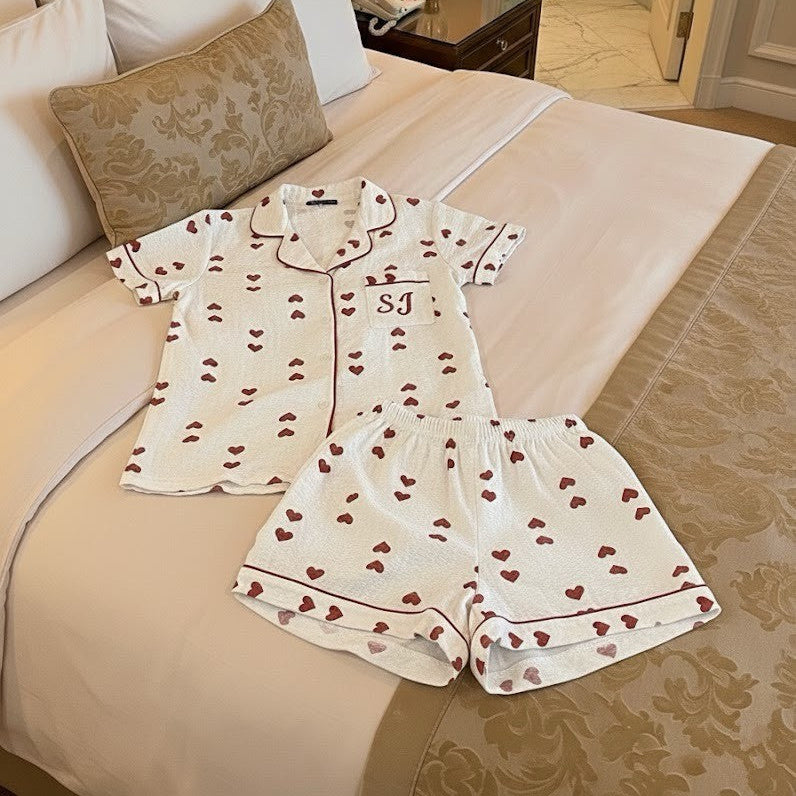 White pajama set with red heart patterns on a bed in a bedroom.