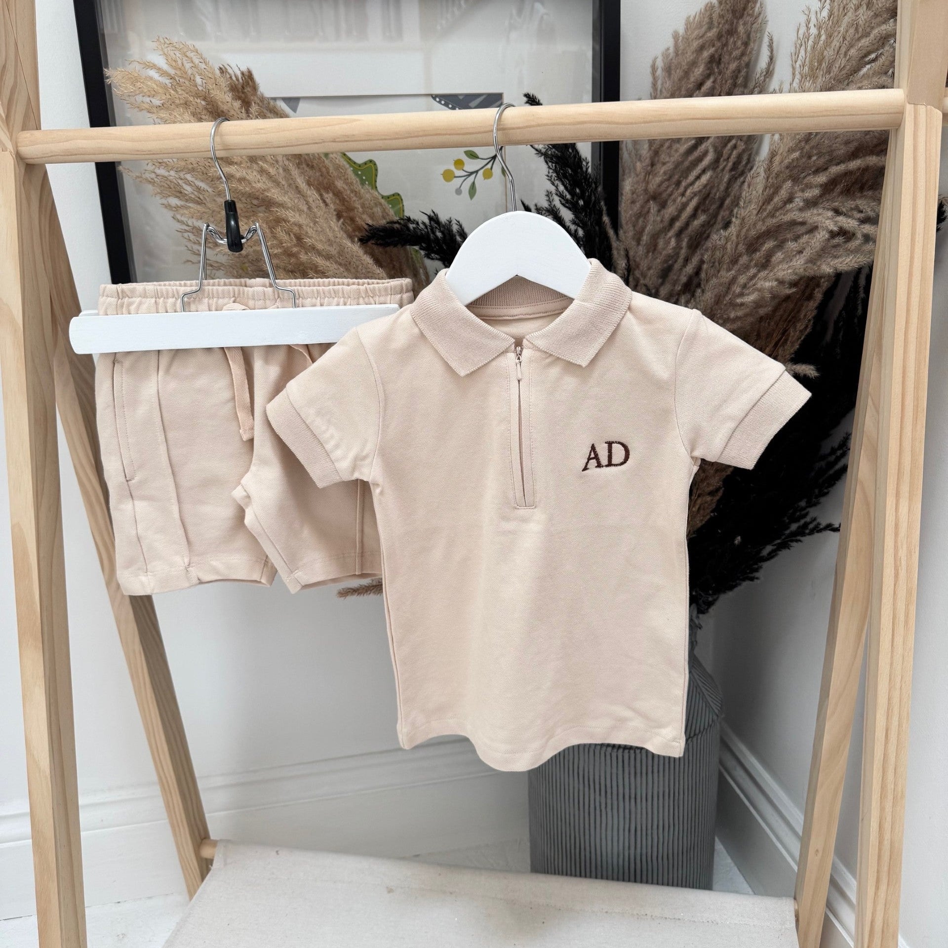 Beige polo shirt with 'AD' logo on a hanger against a neutral background