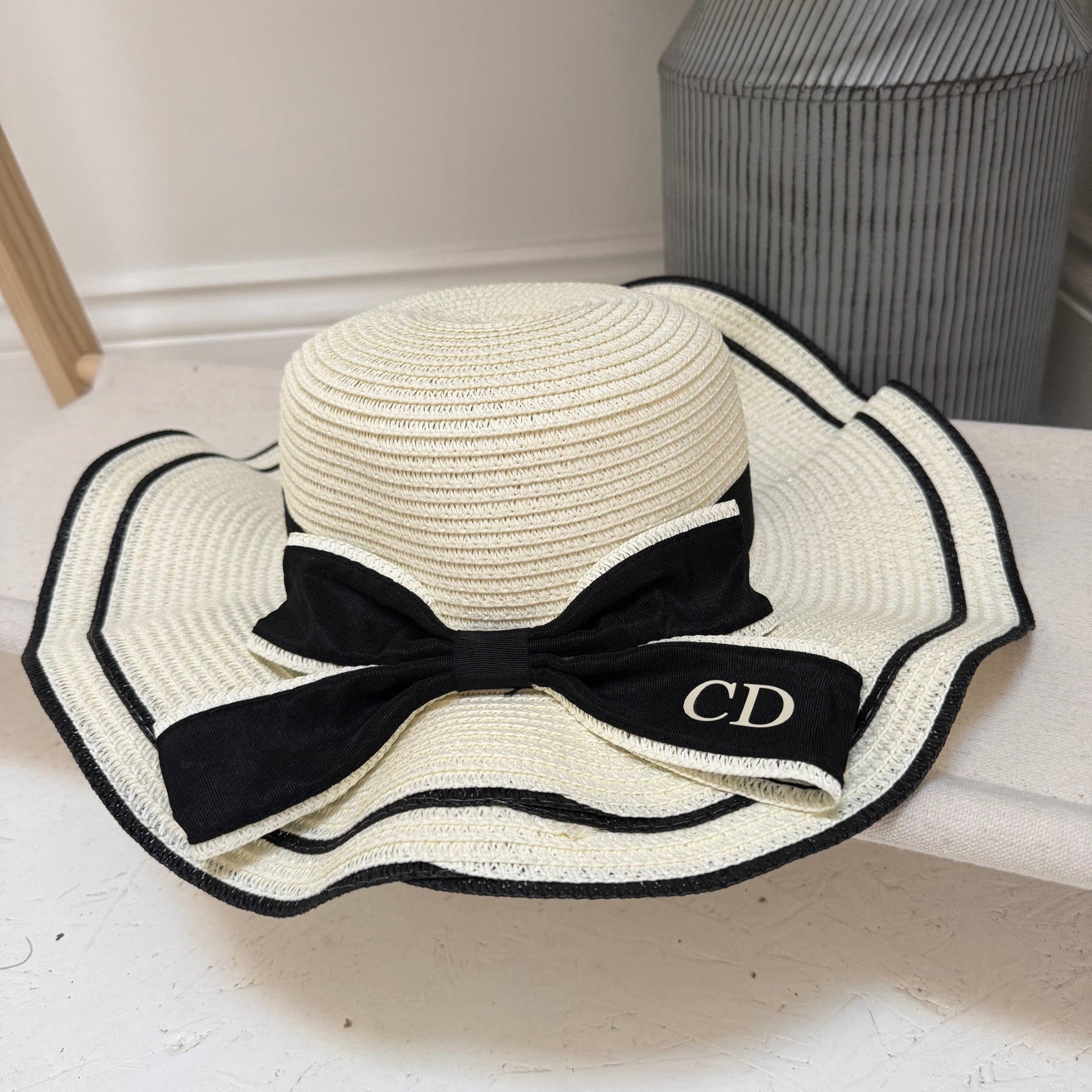 White straw hat with black ribbon and 'CD' logo on a white surface.