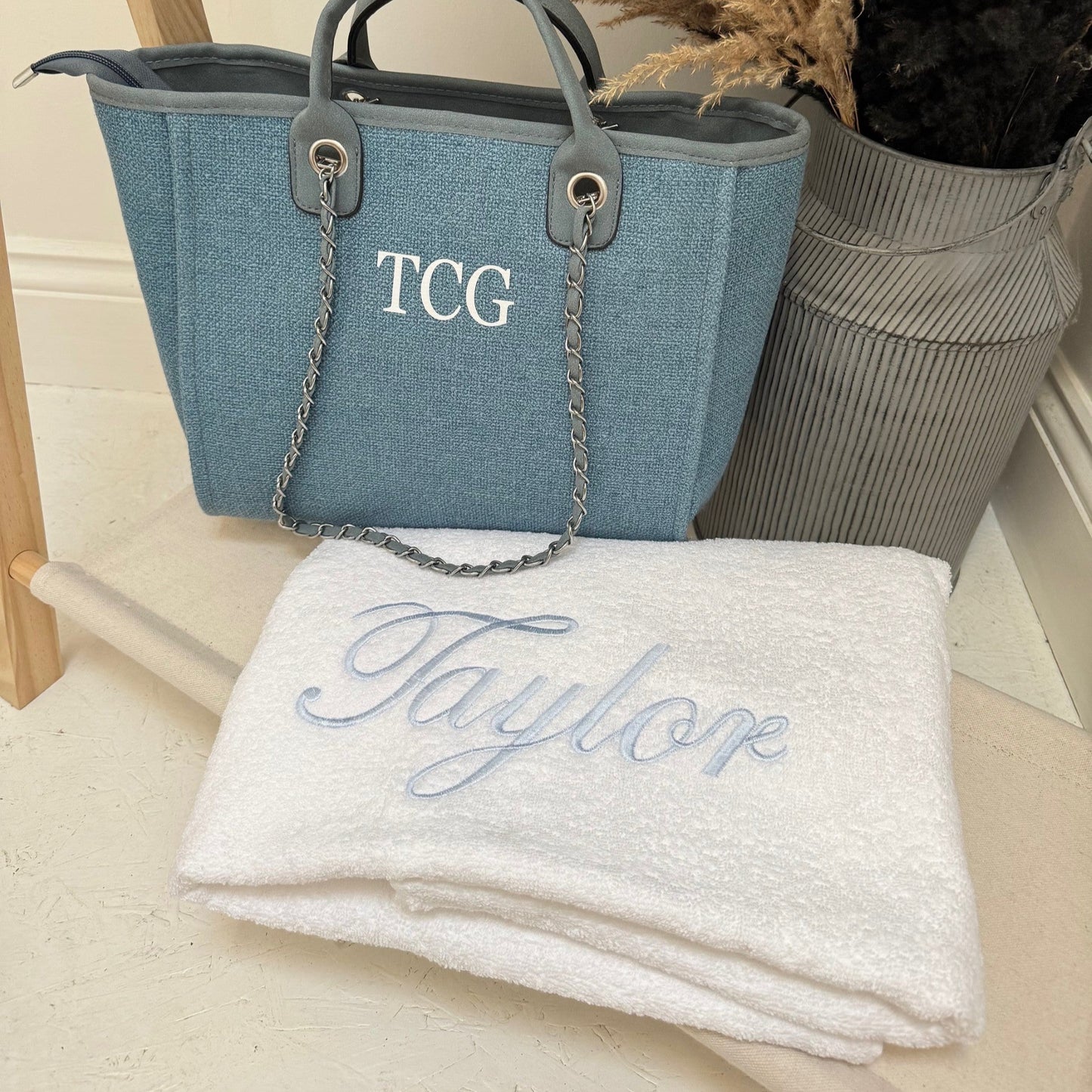 Blue handbag with 'TCG' initials and a white towel with 'Taylor' embroidery on a light surface.