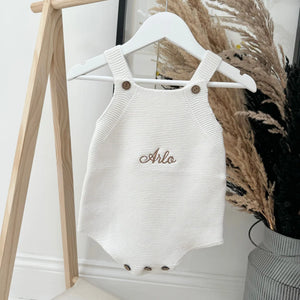 White knitted baby romper with 'Arlo' embroidery on a hanger against a neutral background.